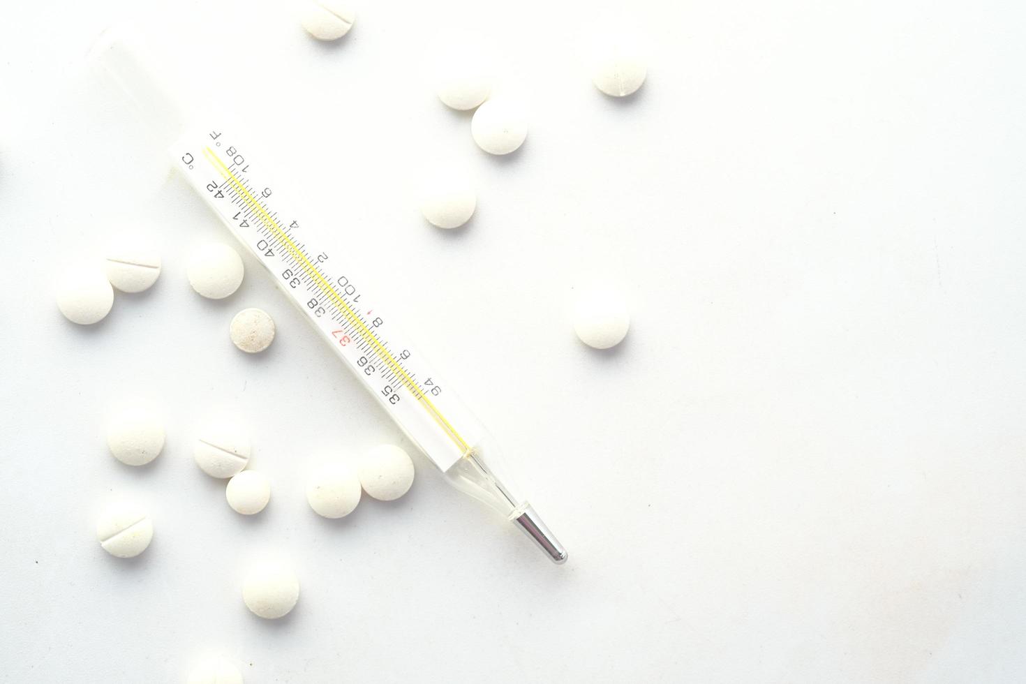 Medical thermometer and pills on white texture background photo
