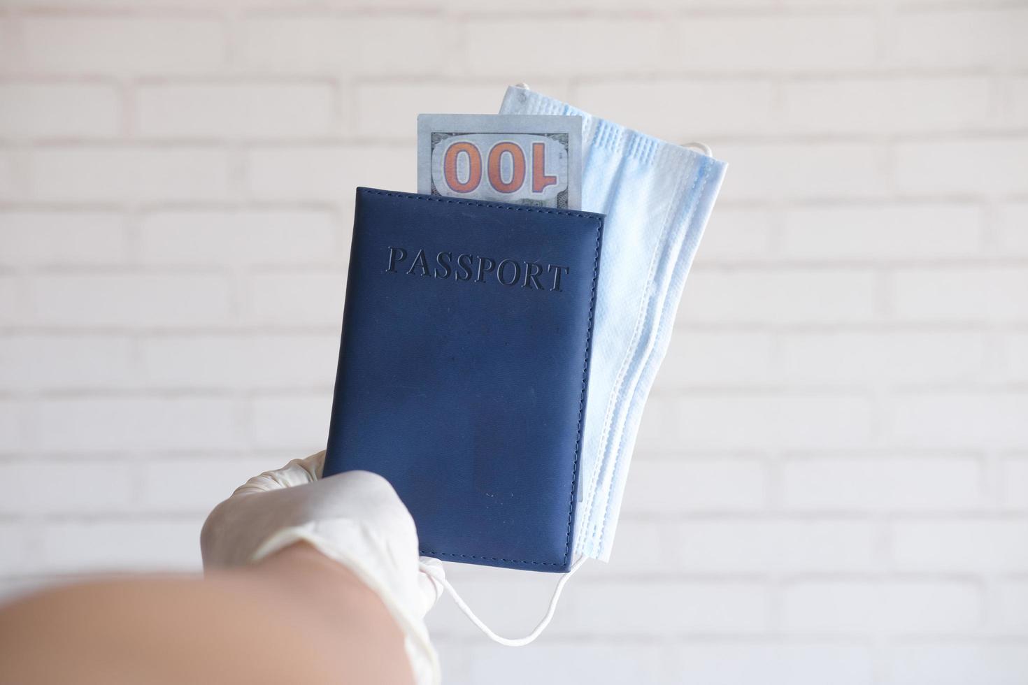 mano en guantes sosteniendo y pasaporte de color azul, efectivo y máscara foto