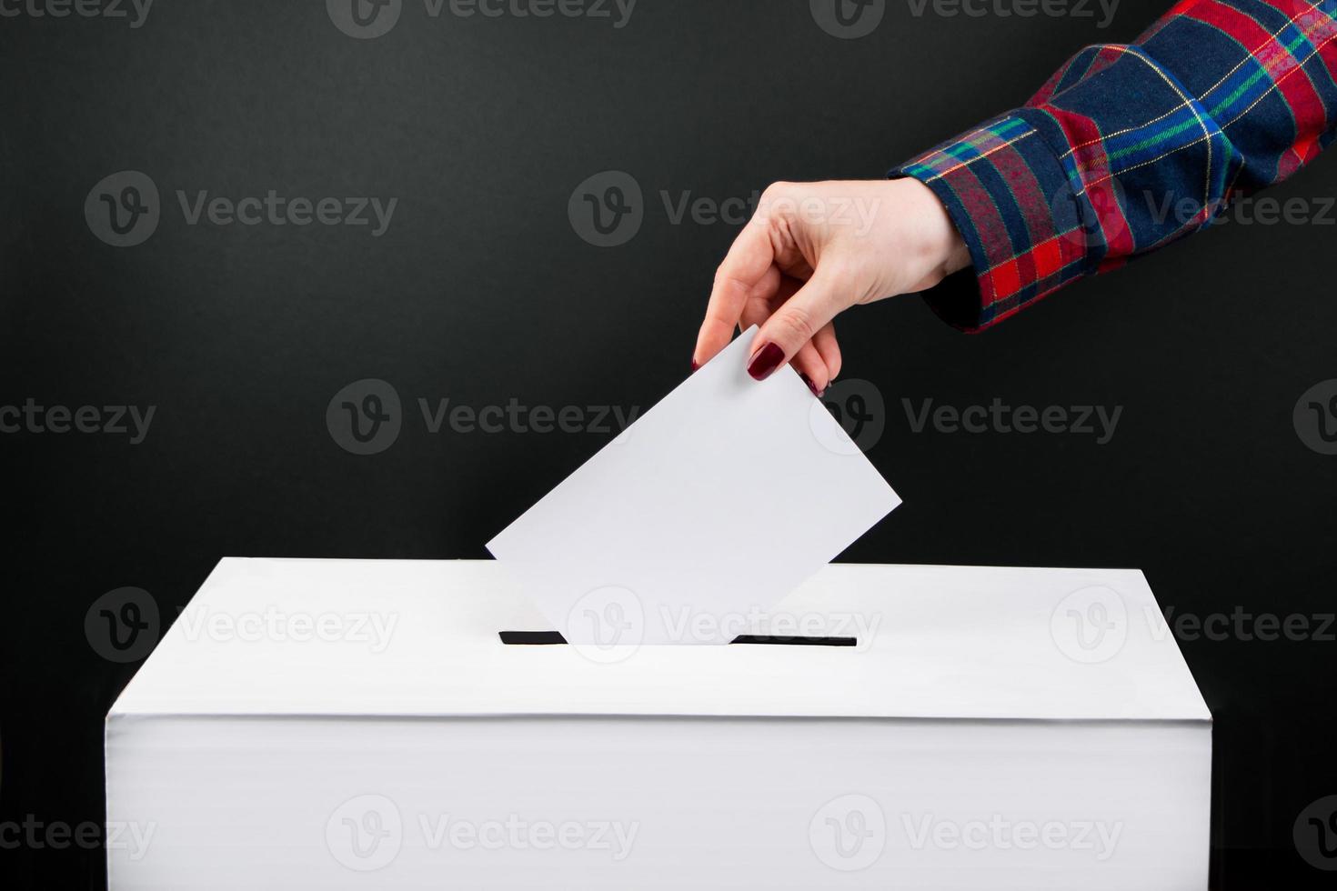 Elections and voting concept. Woman puts ballot paper in box on a black background. photo