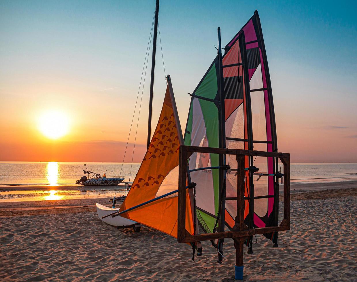 Multi colored windsurfing sails and motor boat on empty beach at dawn during beautiful ocean sunrise at Rivazzurra Rimini Italy adriatic coastline photo