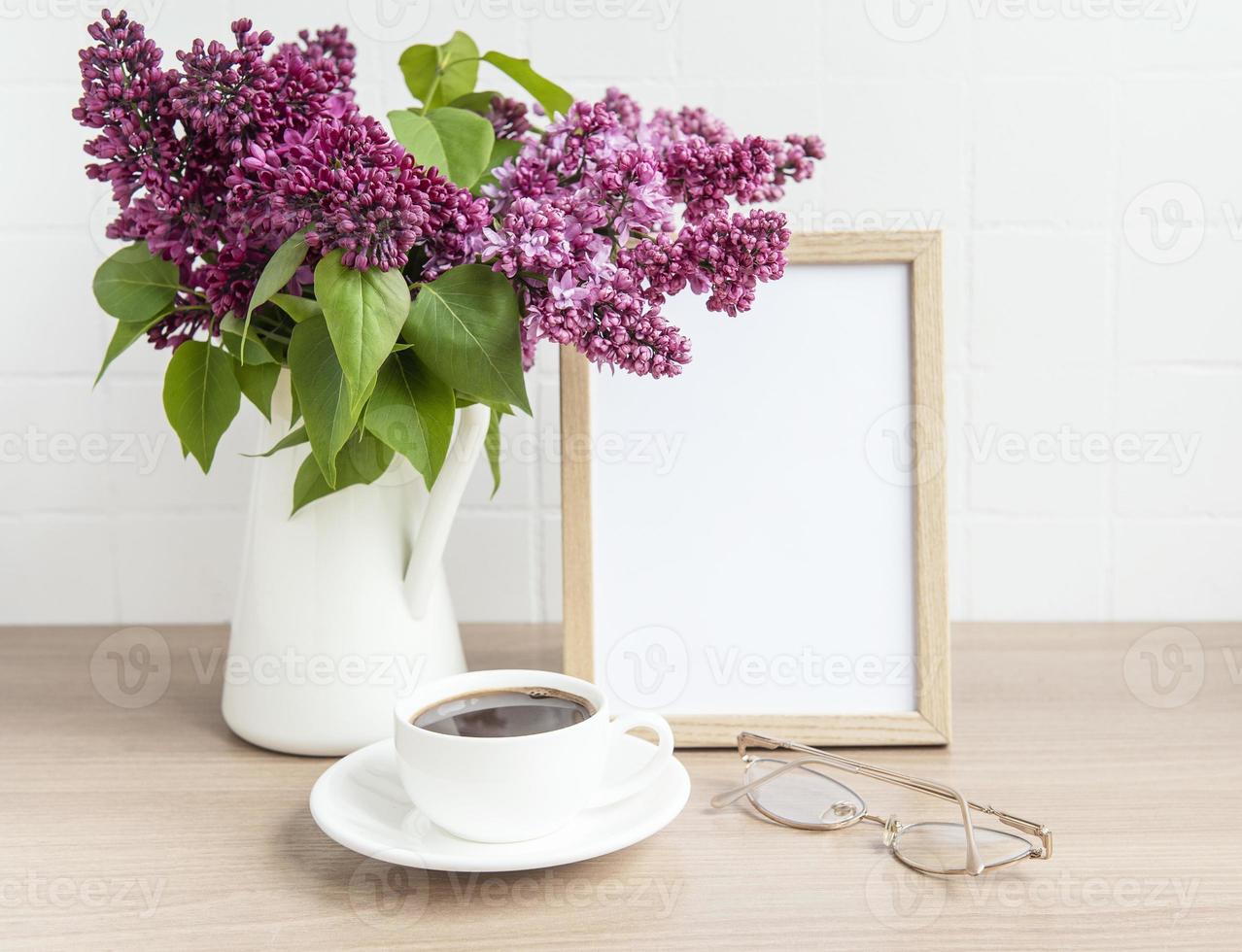 ramo de flores lilas en un jarrón y marco de madera vacío foto