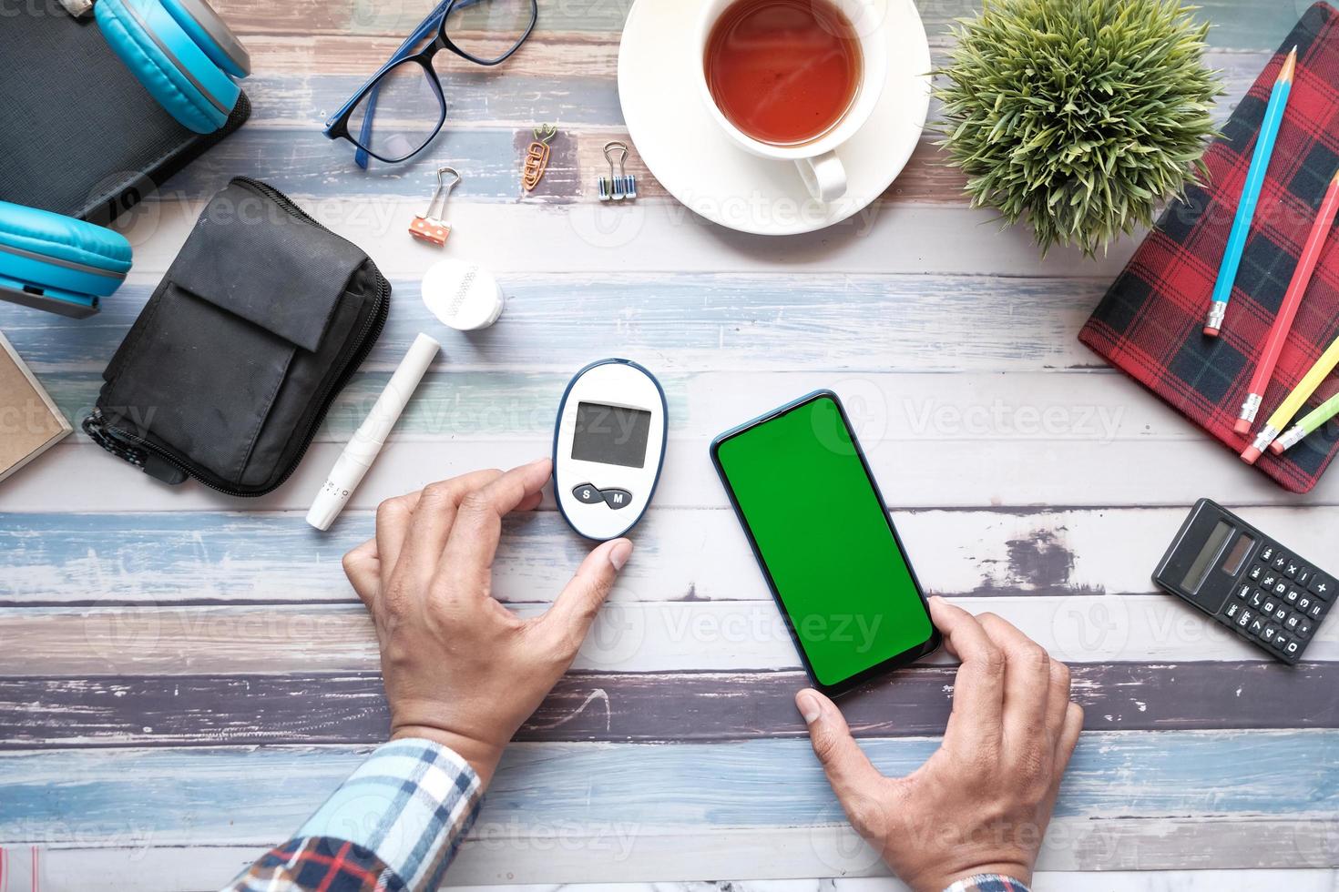 La mano del hombre sujetando el medidor de glucosa y el teléfono inteligente en la mesa foto