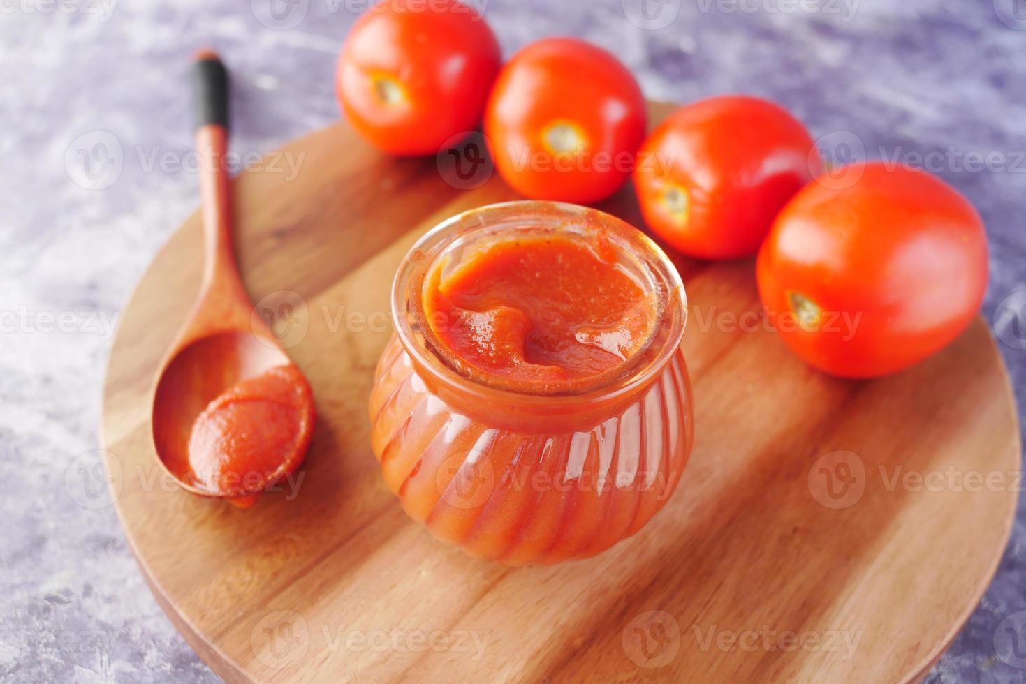 Tomato sauce in a small jar with fresh tomato on table photo