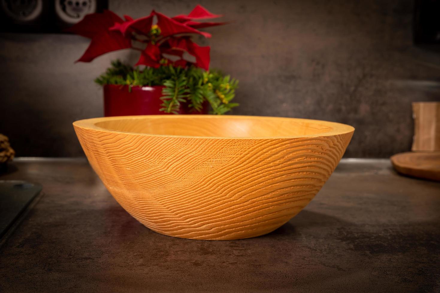 A turned rustic light wooden bowl stands on a dark surface photo