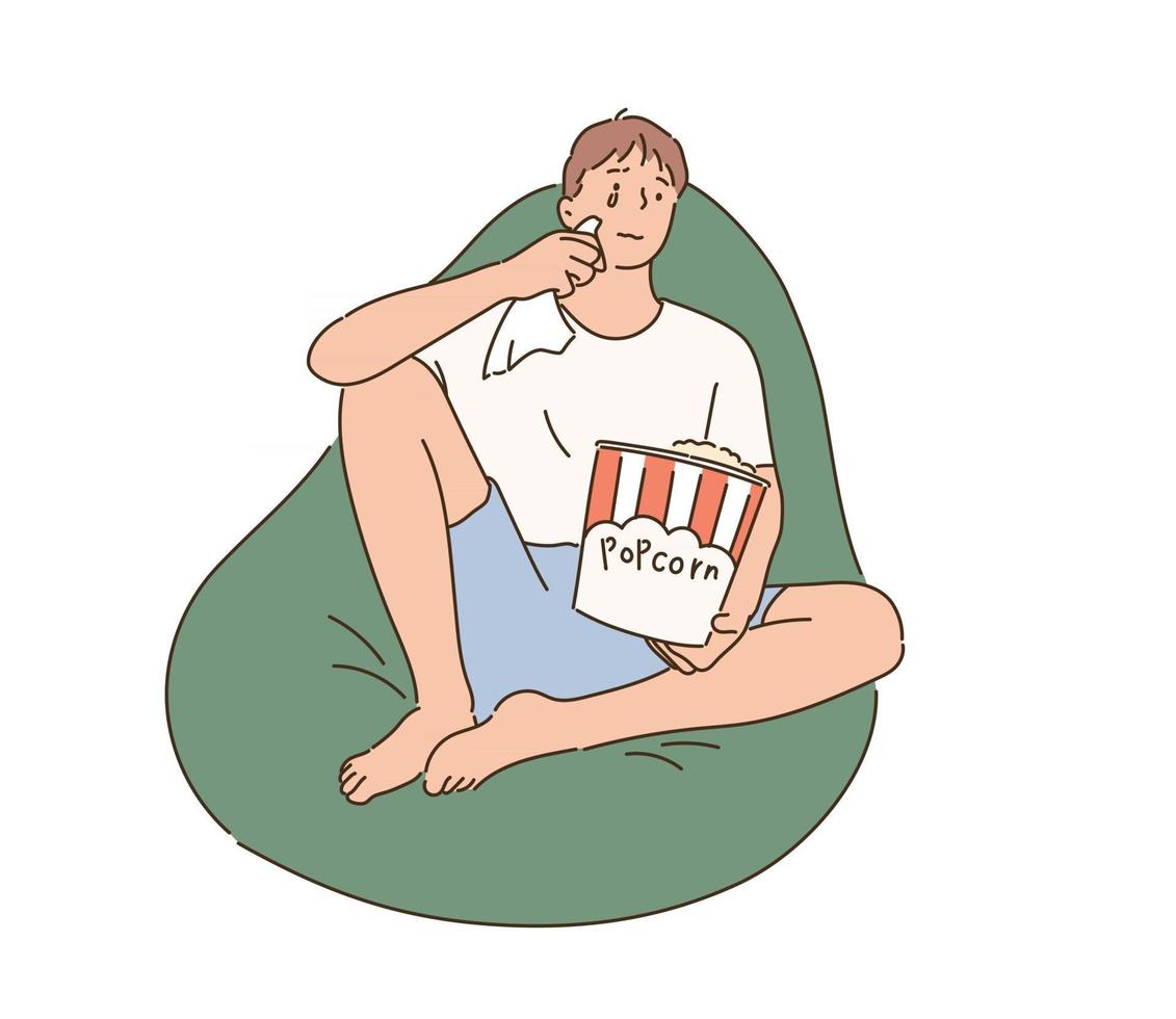 A man is sitting on a beanbag, eating popcorn and watching a sad movie. hand drawn style vector design illustrations.