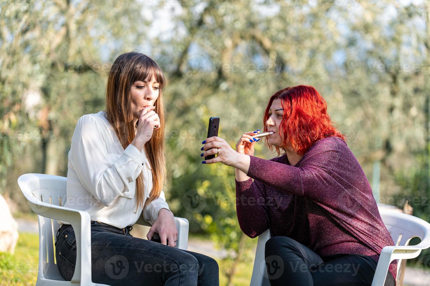 amigas usando teléfonos inteligentes y fumando cigarrillos foto