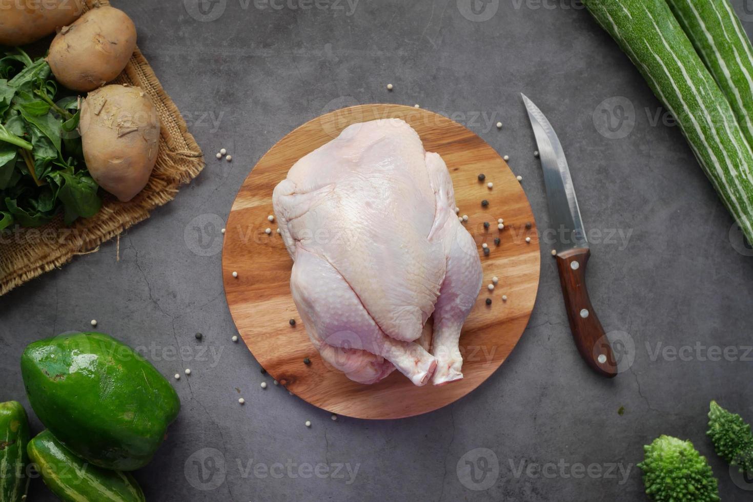 Pollo entero crudo sobre una tabla de cortar con verduras frescas foto