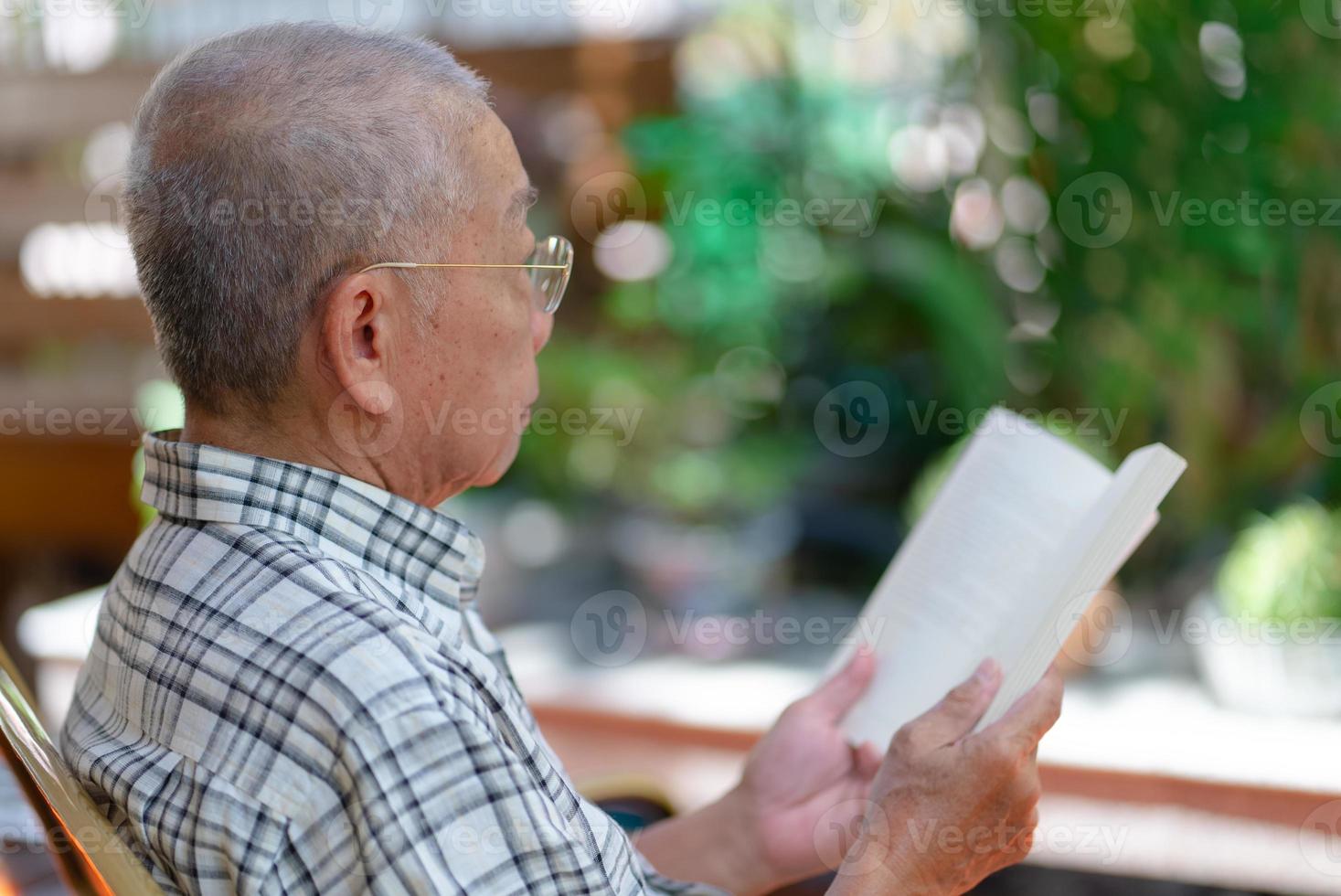 Senior Asian retired man sitting on bench and reading book at home backyard during free time photo