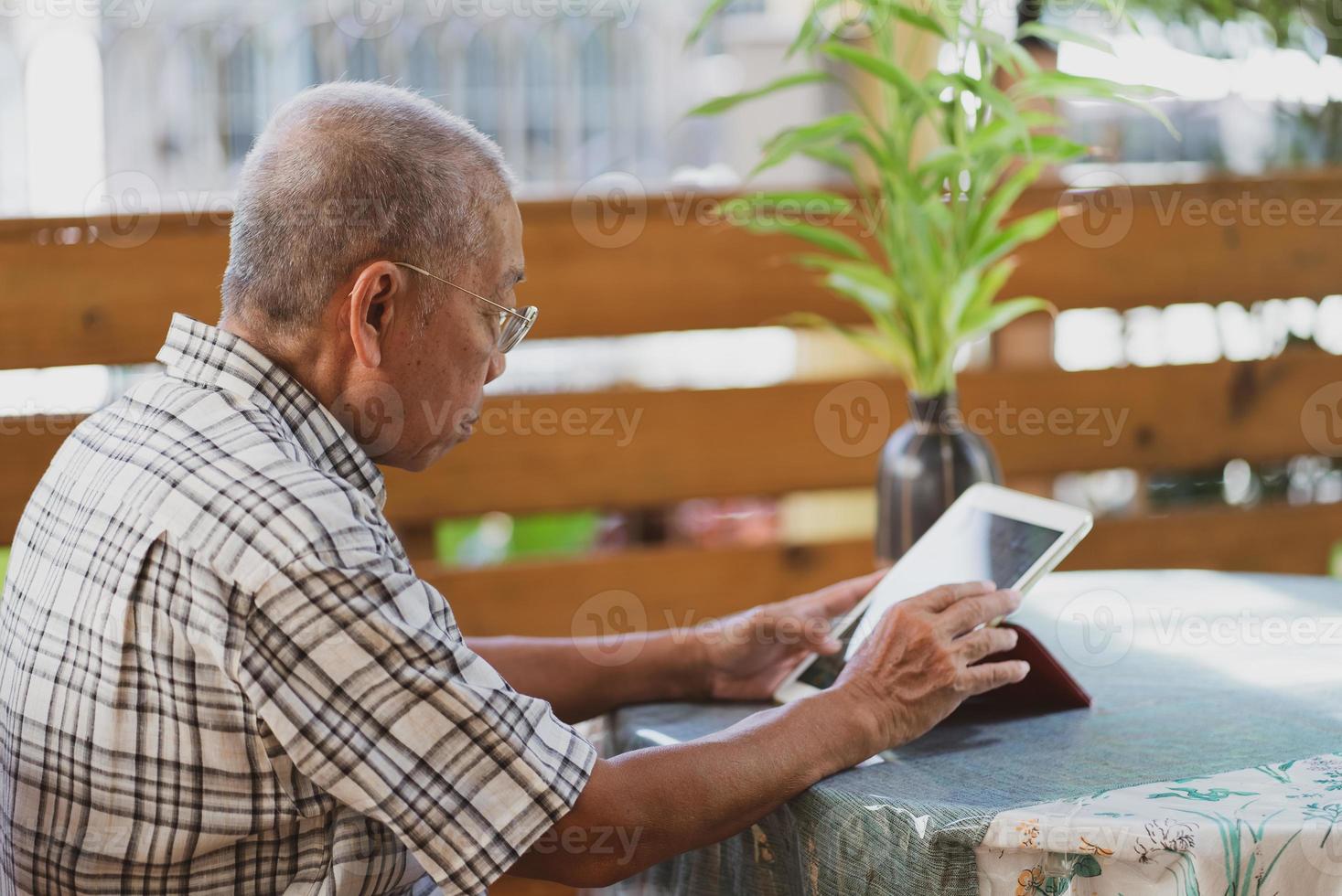 Hombre asiático senior que usa la tableta para reproducir las redes sociales en casa durante el tiempo libre foto