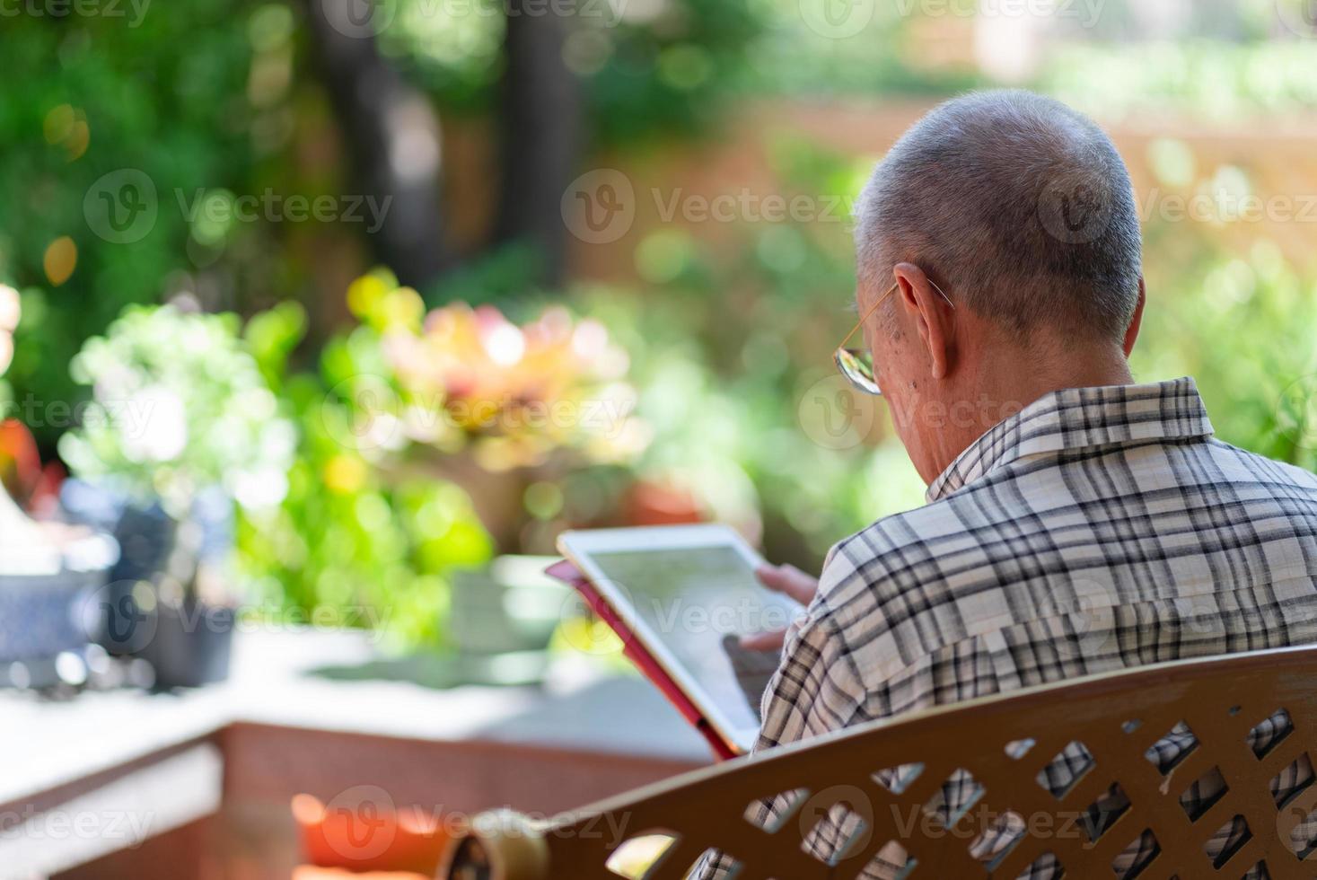 Senior Asian man using tablet to play social media at home during free time photo