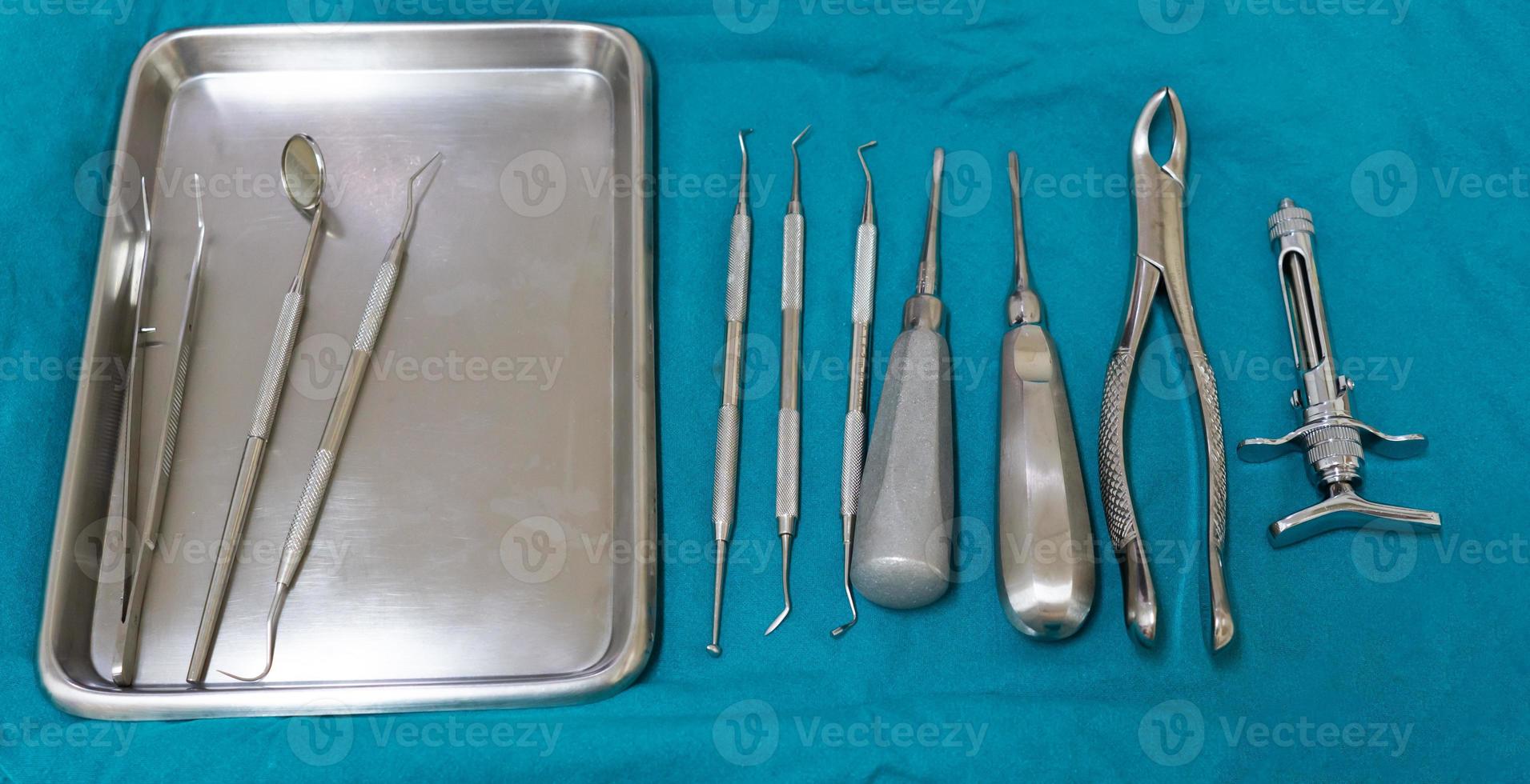 Dental tools including cotton pliers, mouth mirror, probe, syringe, gracey curette, scaler and extraction forcep on the sterile green fabric reaady for operation. dentistry and dentist concept photo