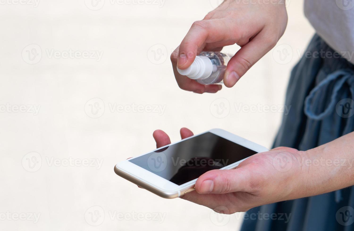 Woman spraying phone with disinfectant photo