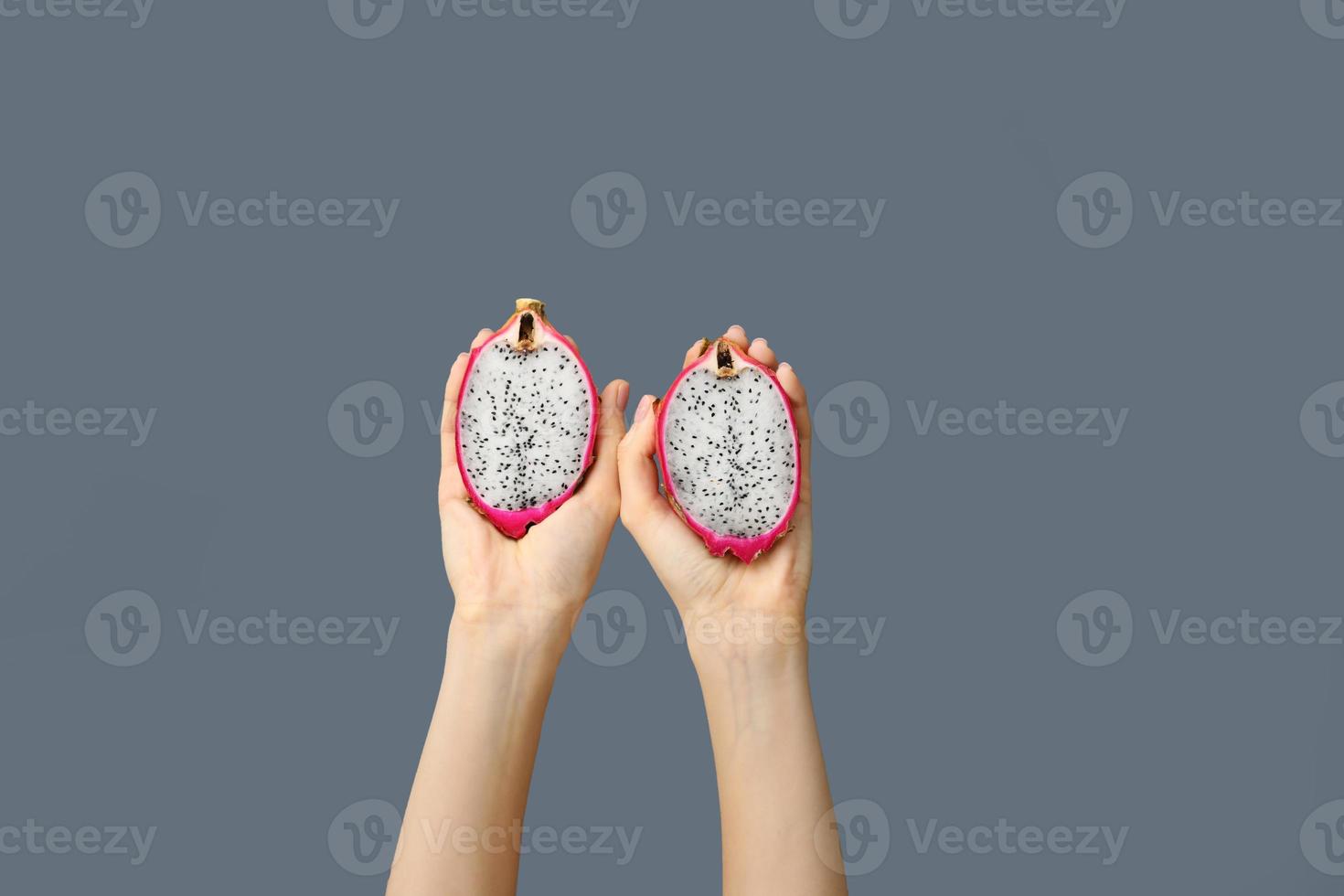 Female hands holding two half dragon fruit or pitaya on grey background. Idea of Vibrant and Healthy Food. copy space photo