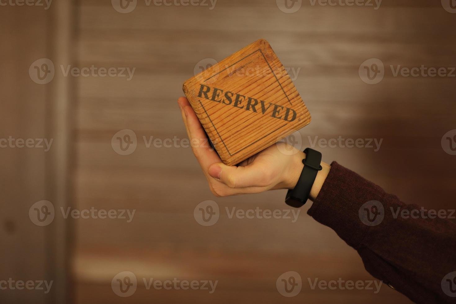A wooden plaque has a word reserved . male hand holds a wooden plate with the inscription reserved isolated on a white background. selective focus. photo