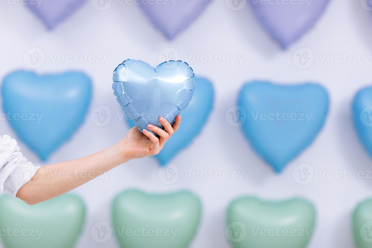 la mujer sostiene el globo azul en forma de corazón en el fondo de muchos corazones. día de San Valentín. enfoque selectivo foto