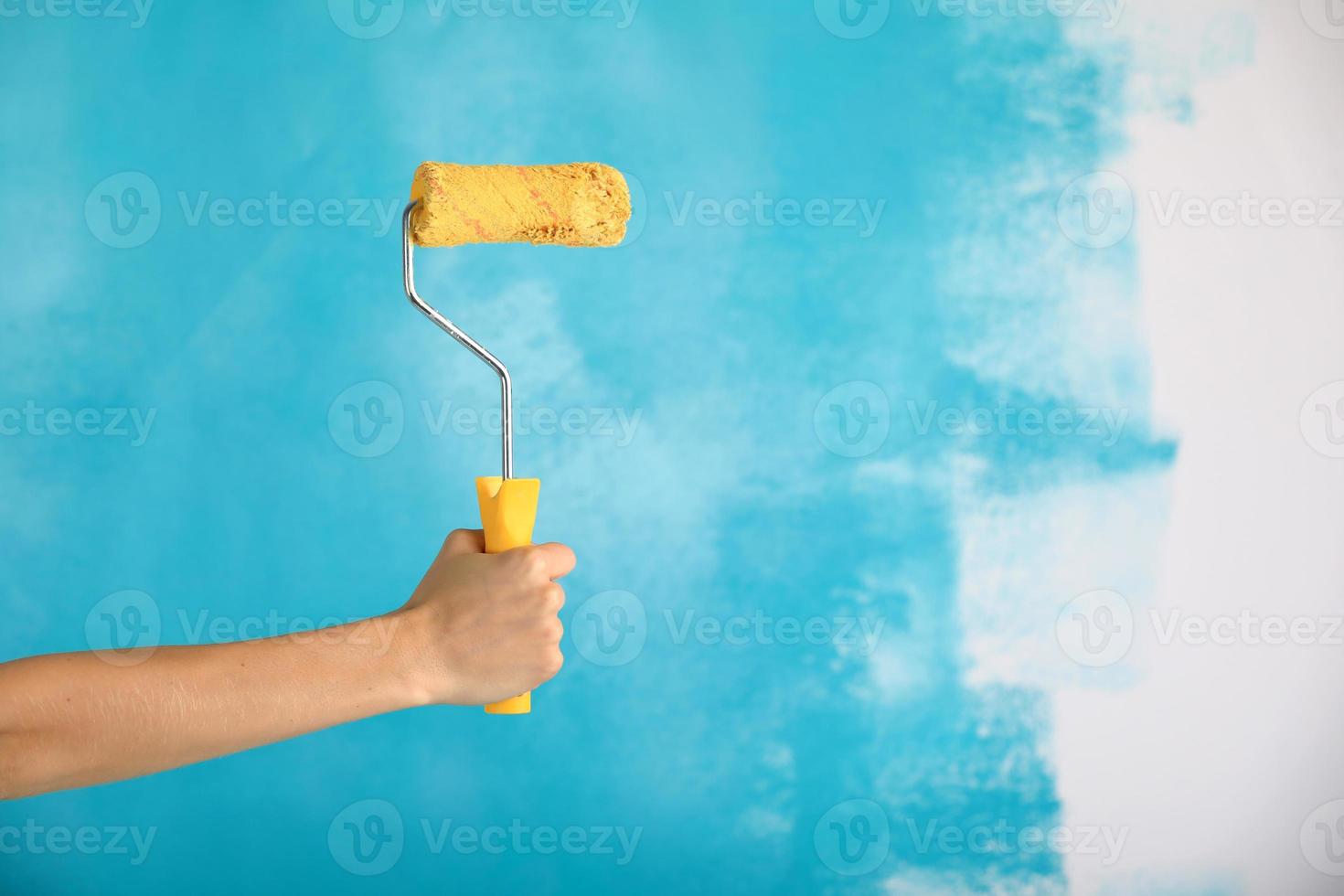 Cerca de la mano femenina sosteniendo el rodillo de pintura amarillo sobre fondo azul. foto