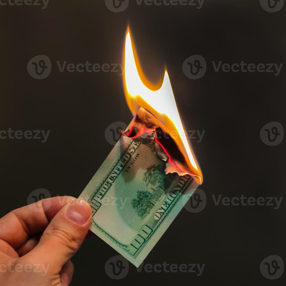 la mano sostiene cien dólares en llamas. Ilustración de la crisis financiera y la pérdida de dinero y capital. foto