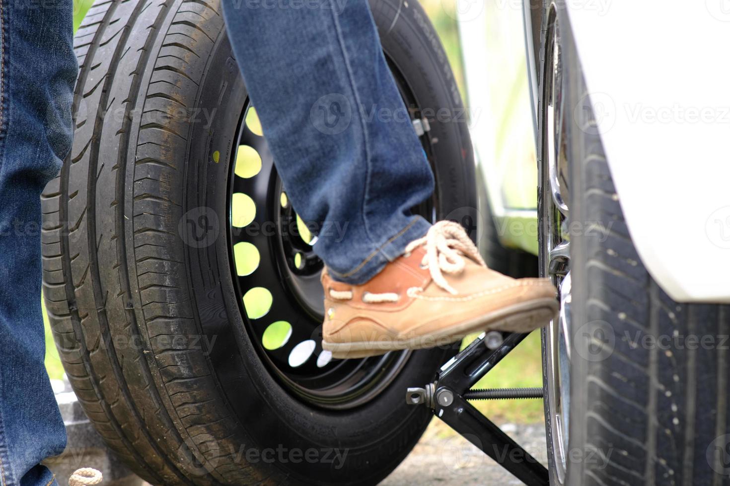 Asian young man sitting on a broken car calling for assistance and repaired wheeled vehicles on the road, Replacing winter and summer tires. Seasonal tire replacement concept photo