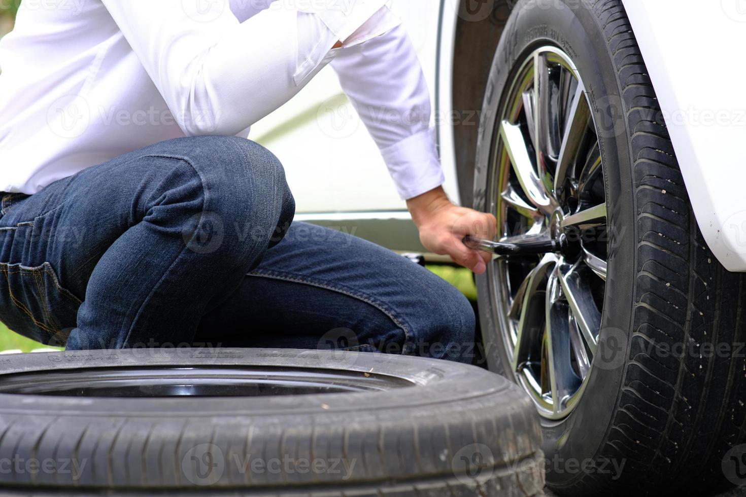 Asian young man sitting on a broken car calling for assistance and repaired wheeled vehicles on the road, Replacing winter and summer tires. Seasonal tire replacement concept photo