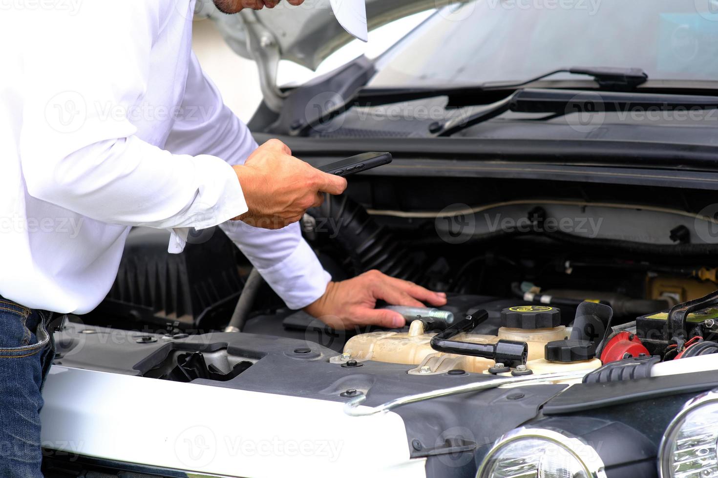 Asian young man sitting on a broken car calling for assistance and repaired wheeled vehicles on the road, Replacing winter and summer tires. Seasonal tire replacement concept photo