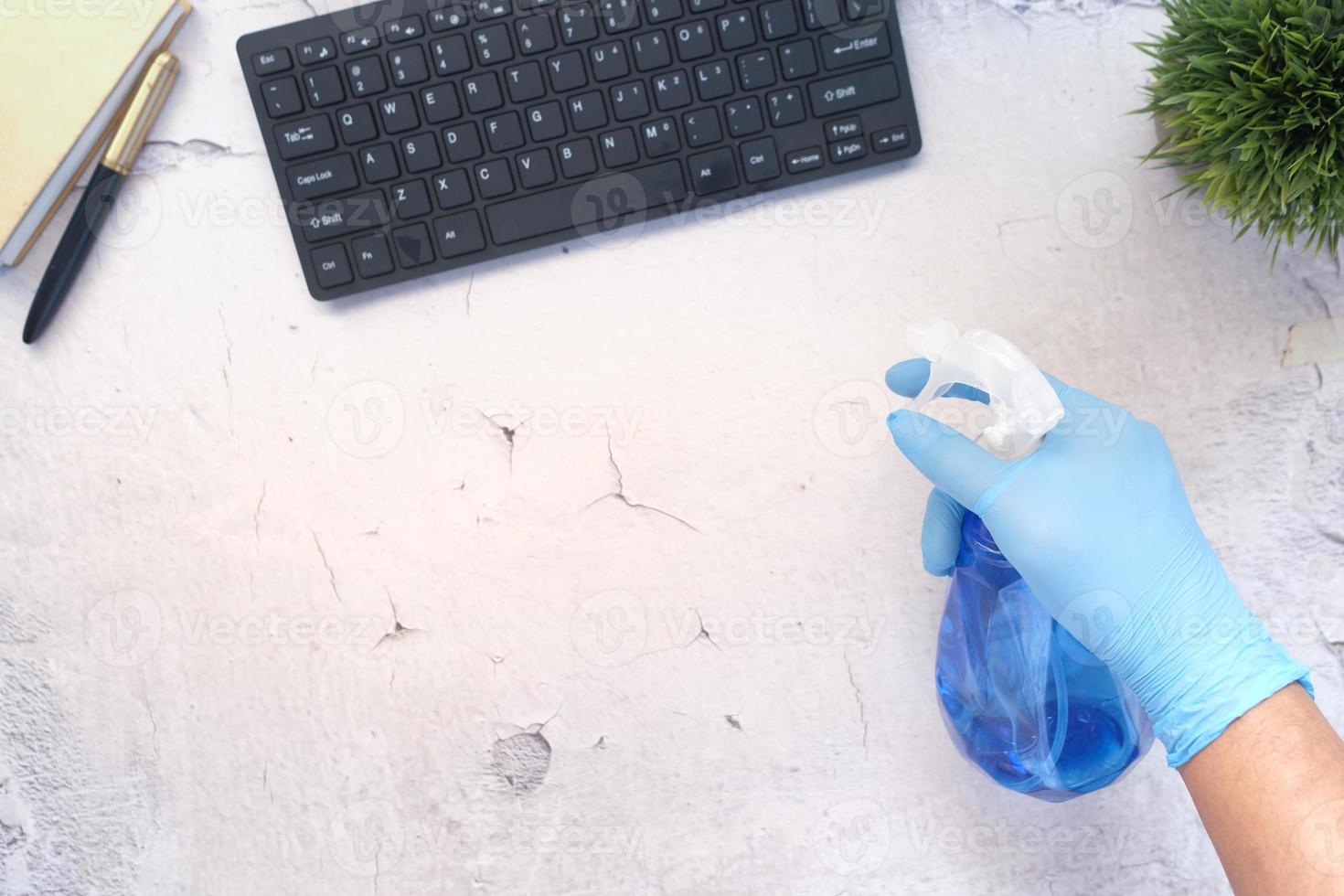 Mano en guantes de goma azul sosteniendo la mesa de limpieza de botellas de spray foto