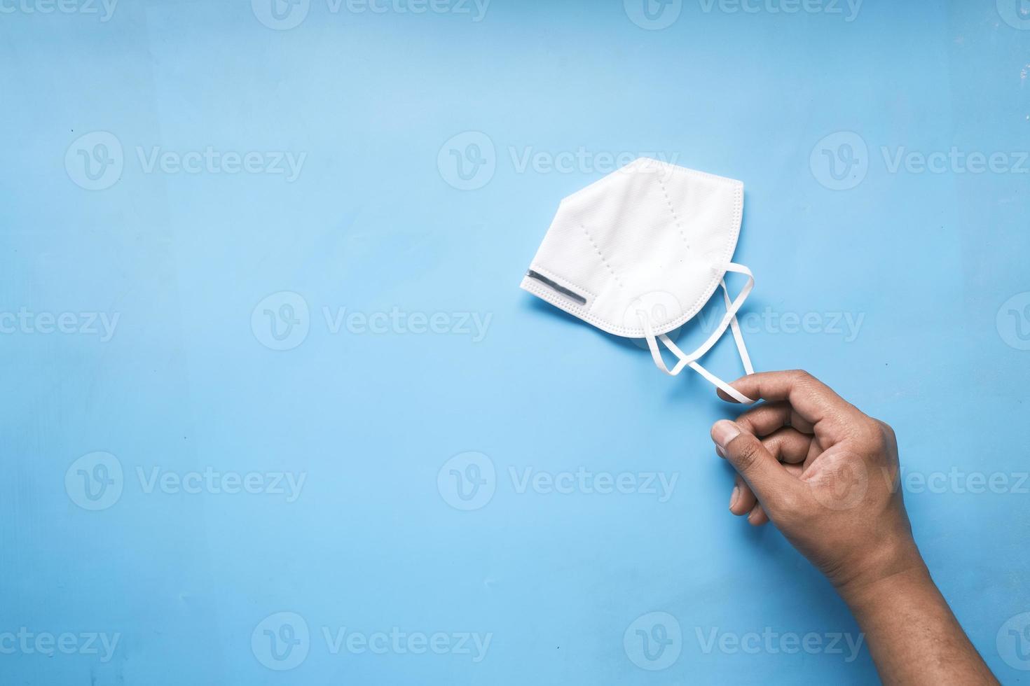 man hand holding surgical face mask on blue background photo