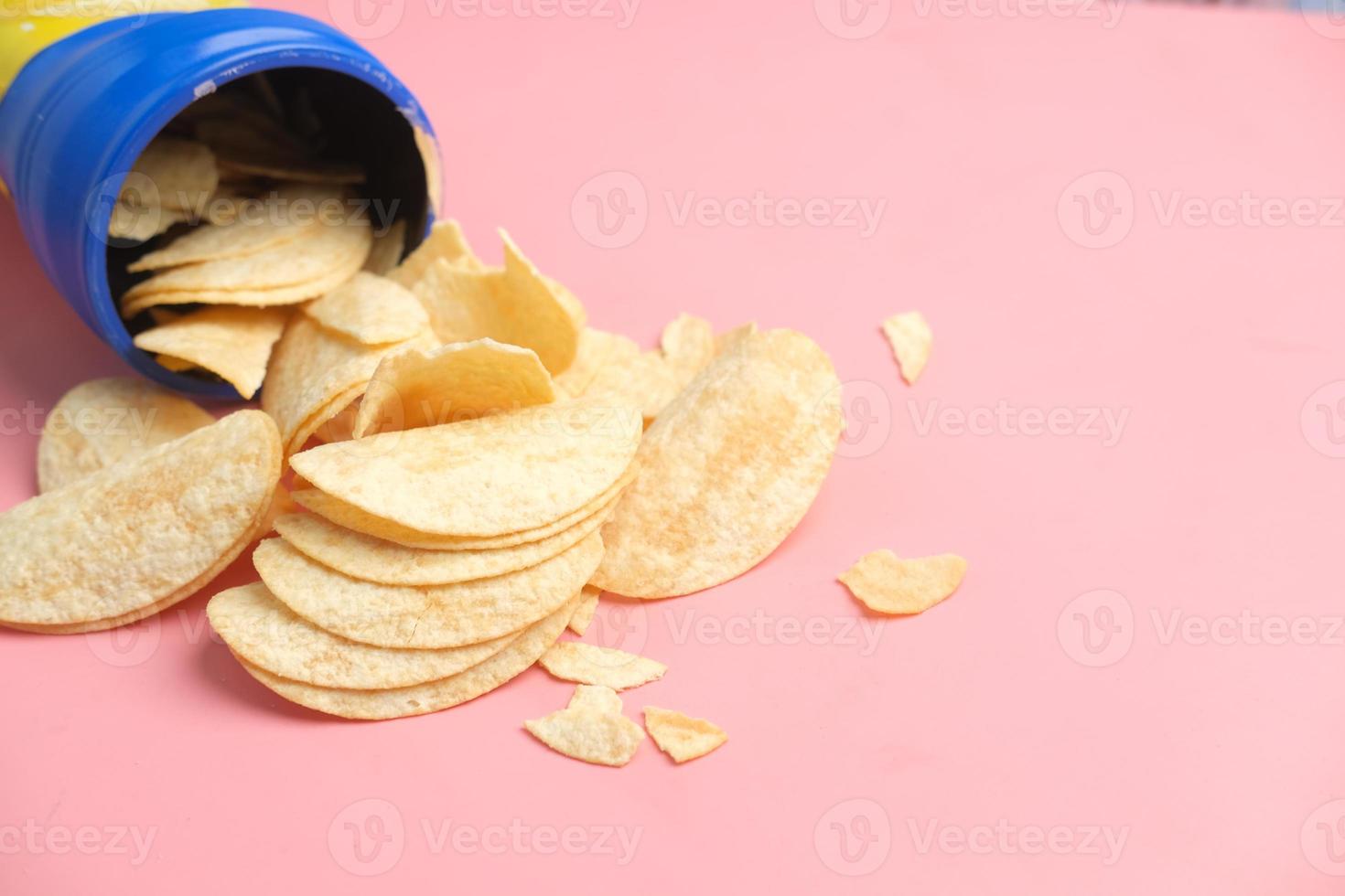 container with tasty potato chips on pink background . photo