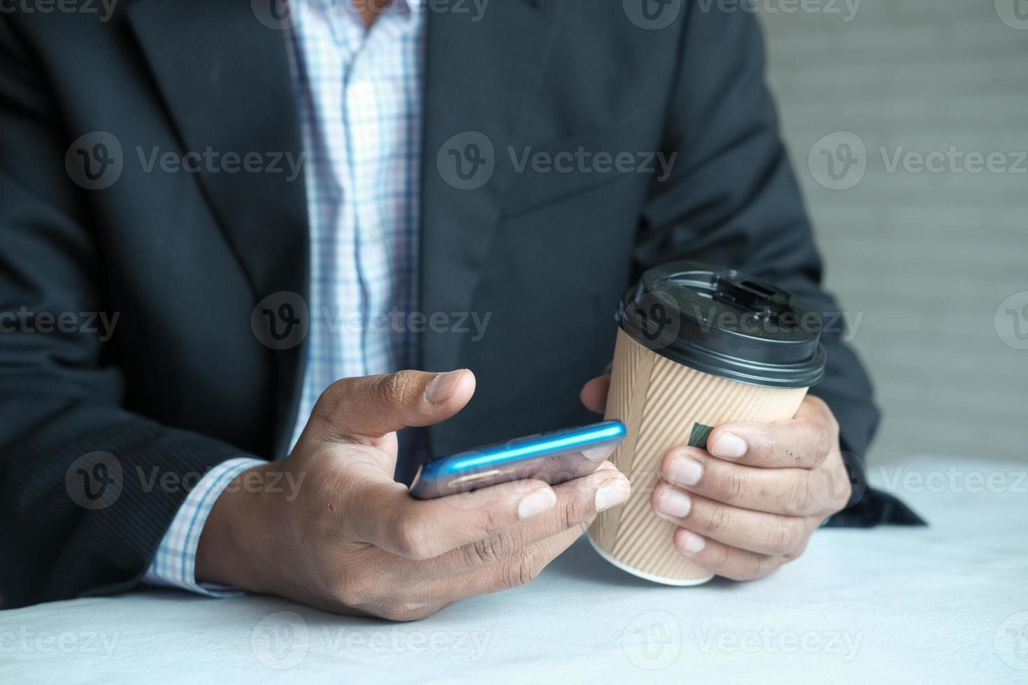 mano de hombre de negocios con teléfono inteligente y taza de café de papel foto