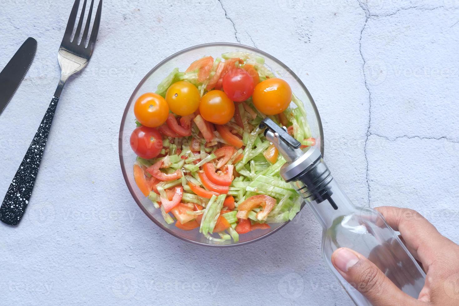 putting olive oil in fresh vegetable salad bowl on table, photo