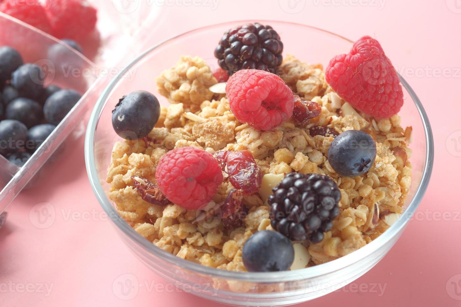 granola y bayas en un tazón sobre fondo rosa foto