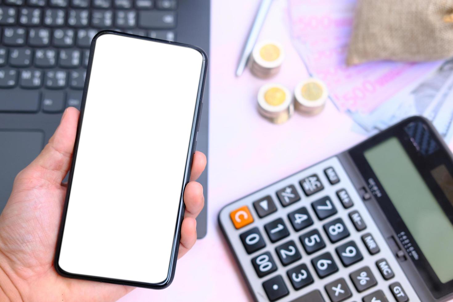 Hand holding smartphone with money on the table and work space, business and technology concept photo