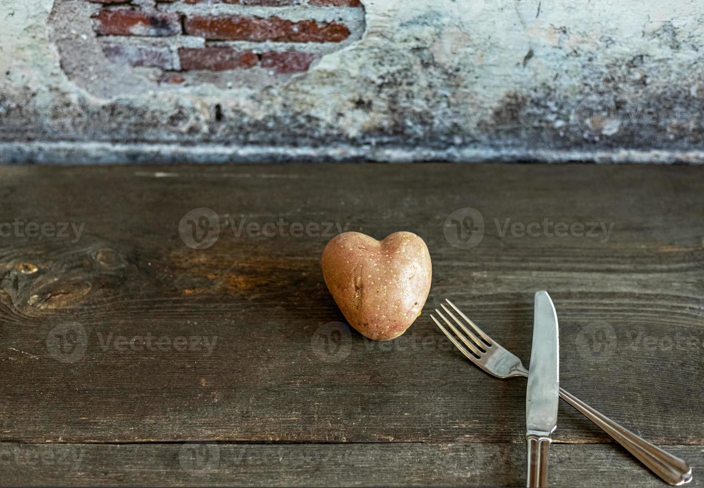 Patata roja en forma de corazón sobre un fondo de madera con un tenedor y un cuchillo foto