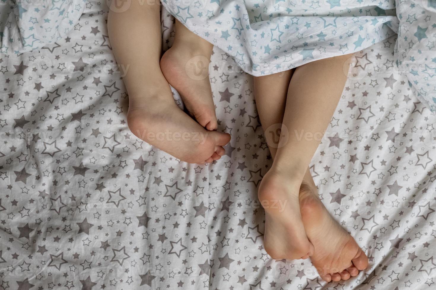 Close-up of two pairs of toddler girls feet on the bed under the blanket photo