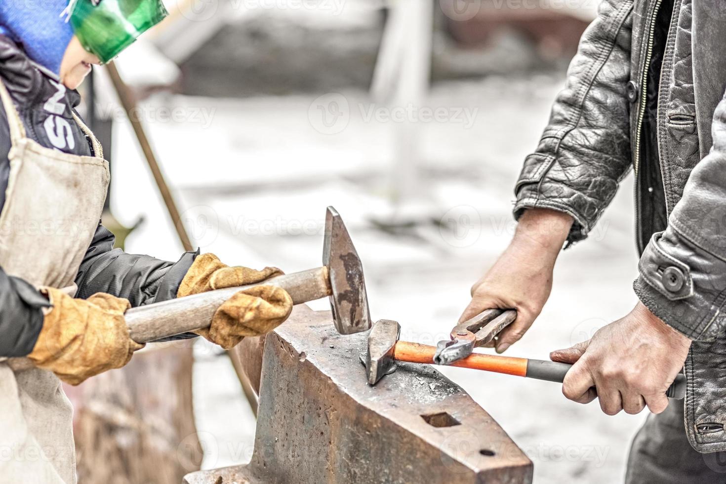 A blacksmith man and his son forge a horseshoe on an anvil photo