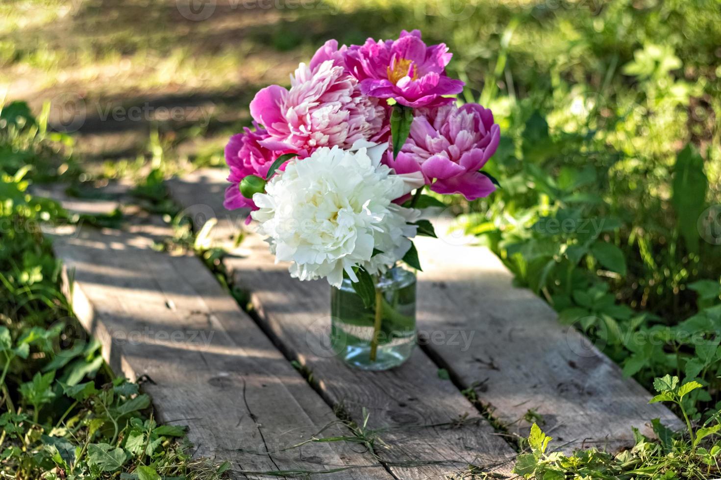 Un ramo de grandes peonías blancas y rosas en un frasco de vidrio sobre un puente de madera foto