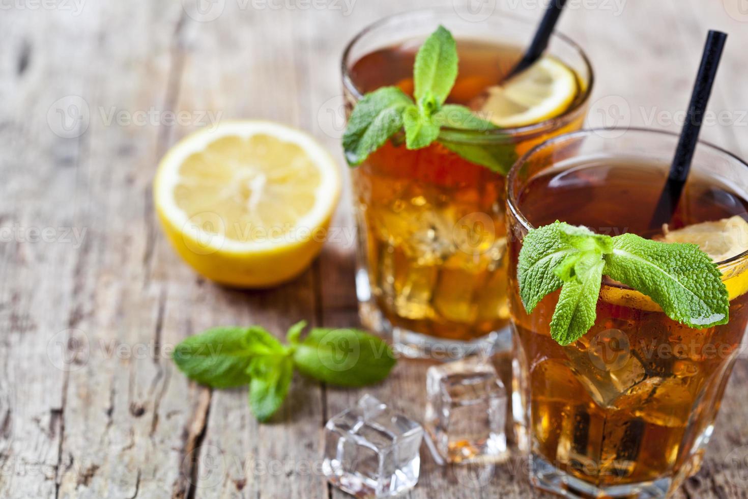 Té helado frío con limón, hojas de menta y cubitos de hielo en dos vasos sobre fondo de mesa de madera rústica. foto