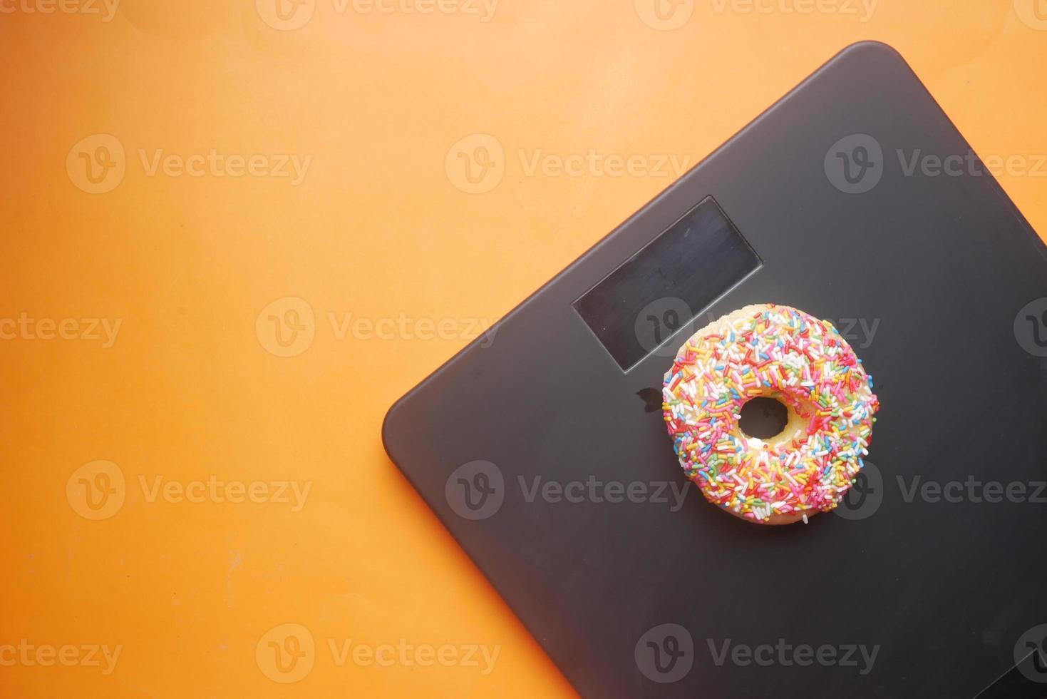 Sweet donuts on weight scale on orange background photo