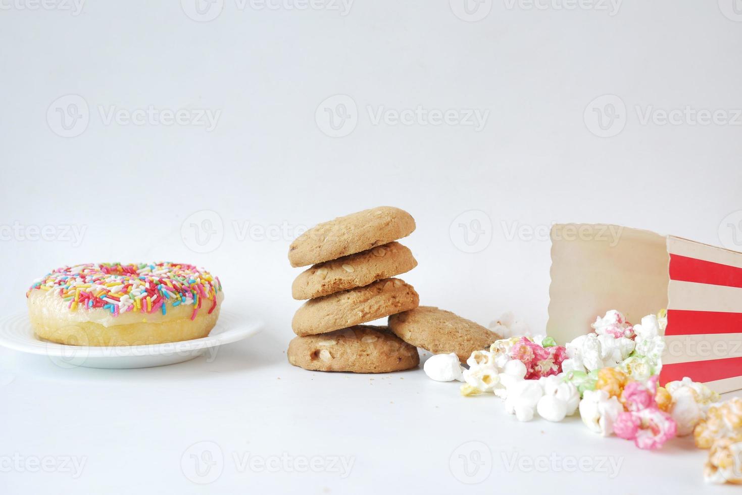 Pila de galletas, donas y palomitas de maíz sobre fondo blanco. foto