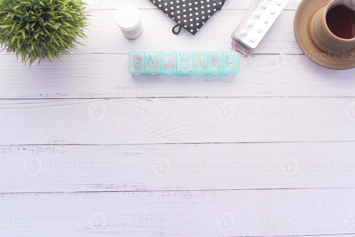 Flat composition of pill box, blister pack and cup of tea on table photo