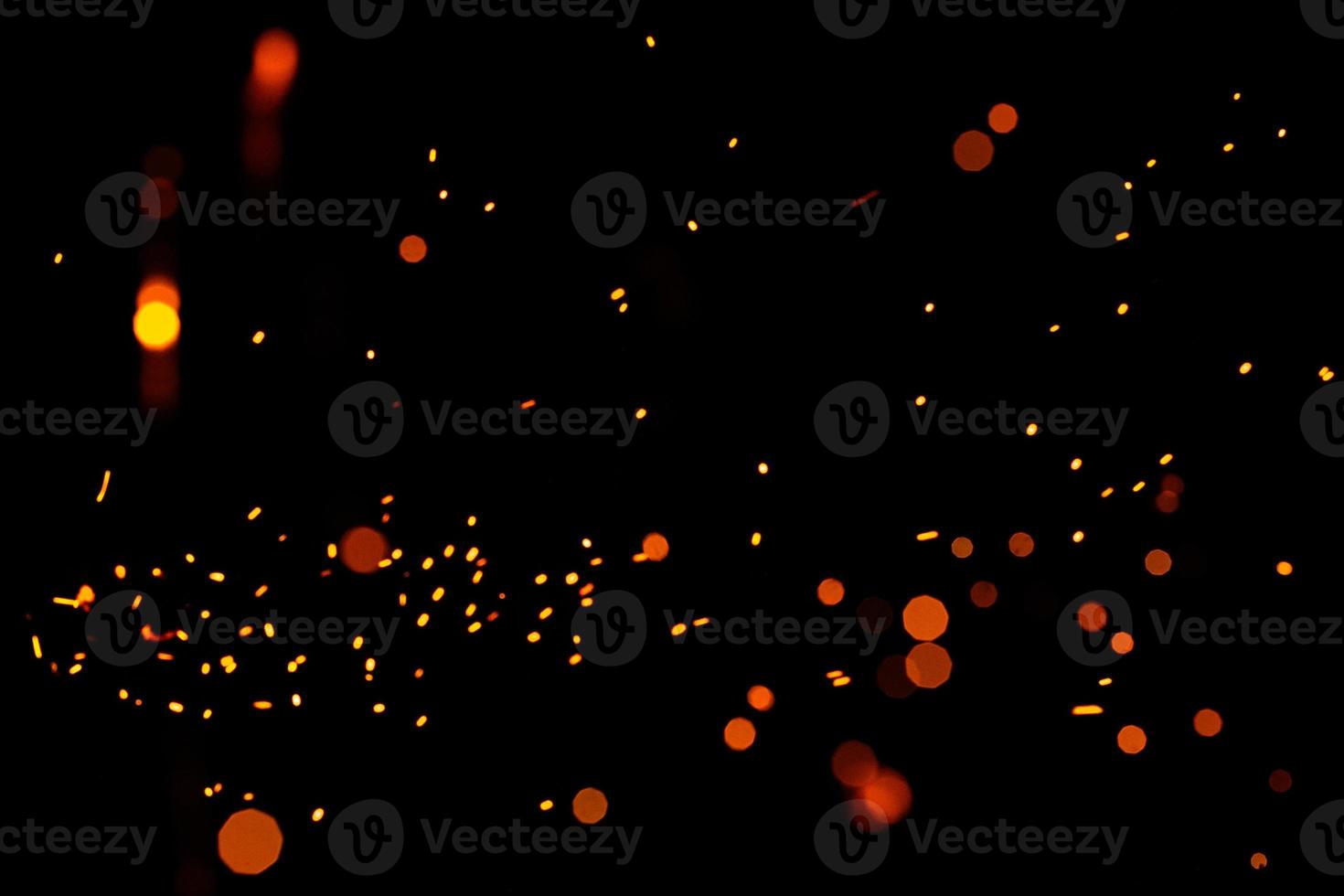 Particles of burning embers fly and glow isolated in the night sky. Bright yellow sparks on a black background, yellow bright round bokeh. photo