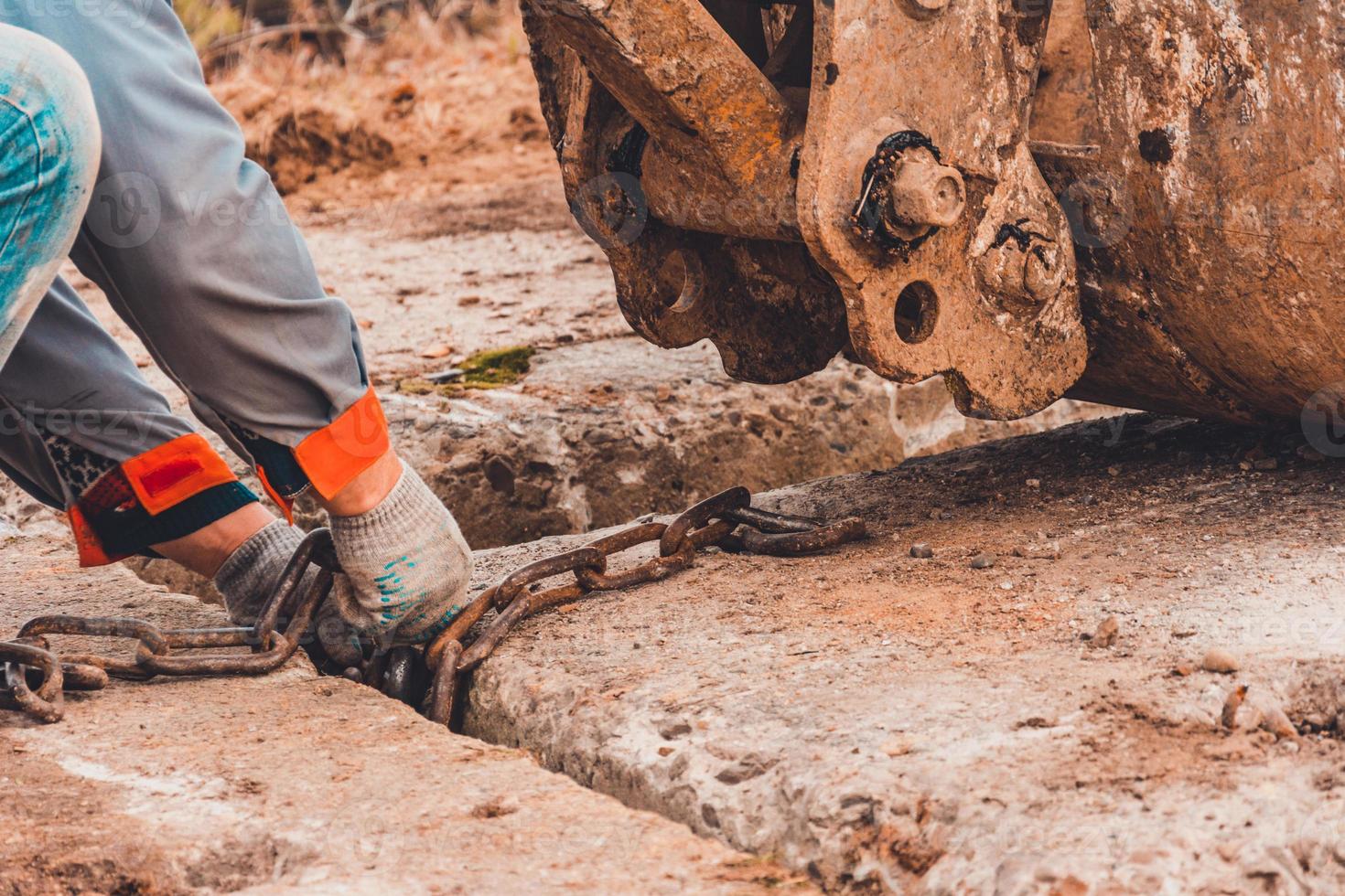 el trabajador sujeta la cadena al cucharón de la excavadora para levantar la losa de hormigón. foto