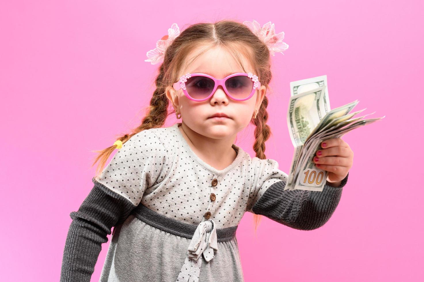 Little girl in glasses with a package and money on a pink background, child and shopping. photo