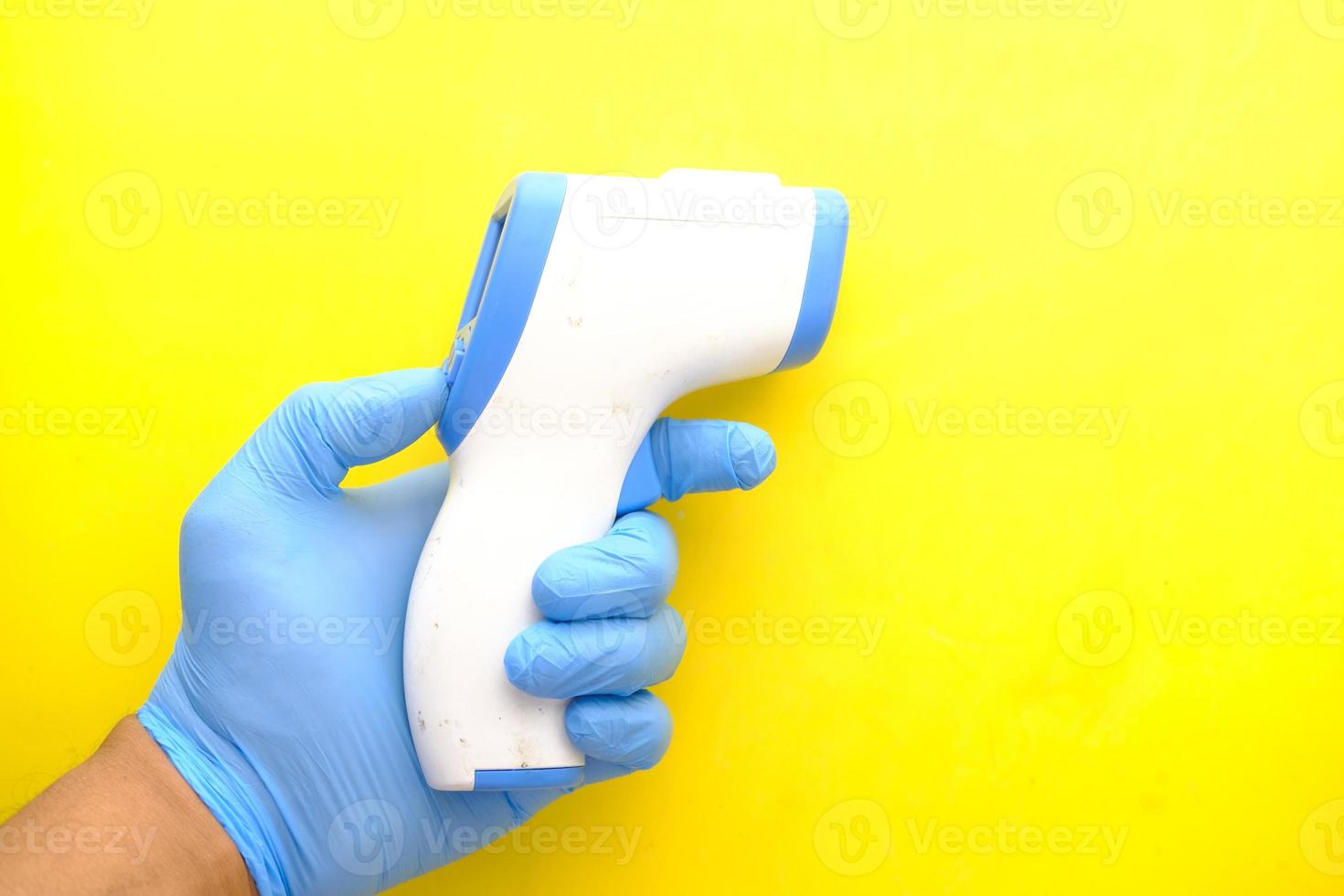 Hand holding infrared thermometer against yellow background photo