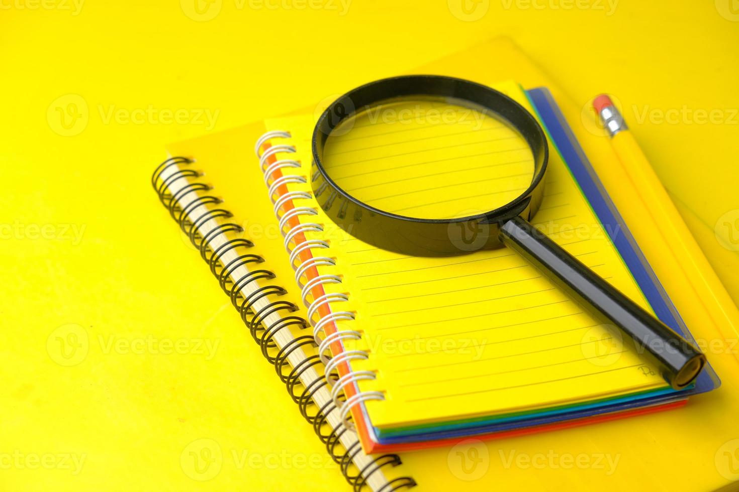 Open notepad and magnifying glass on yellow background photo