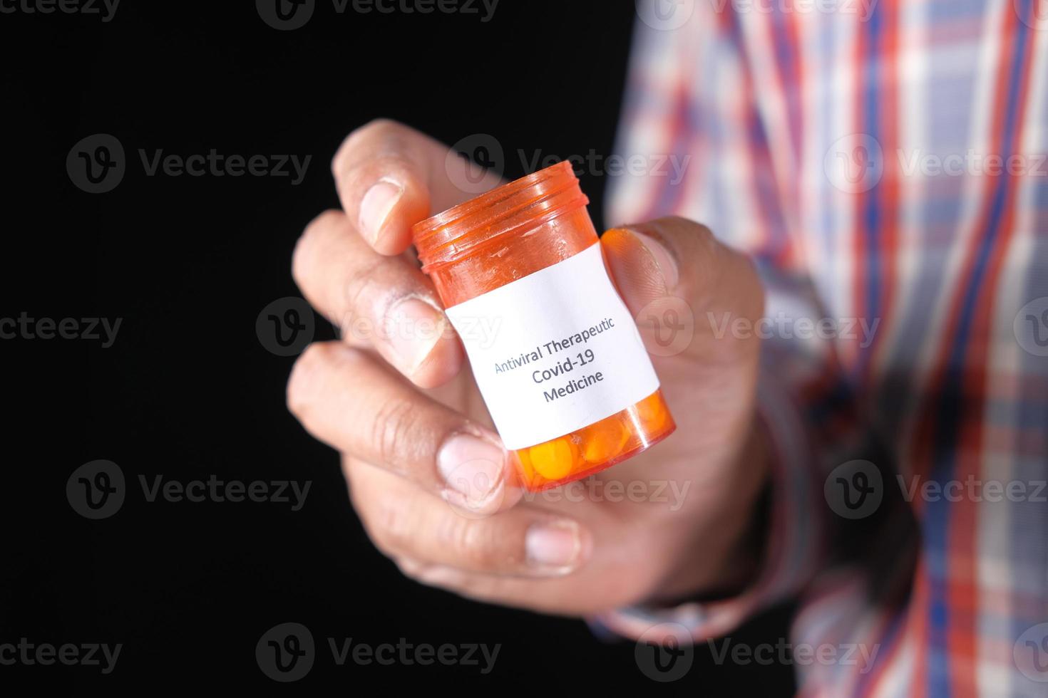 Holding covid 19 medical pills container isolated on black background photo