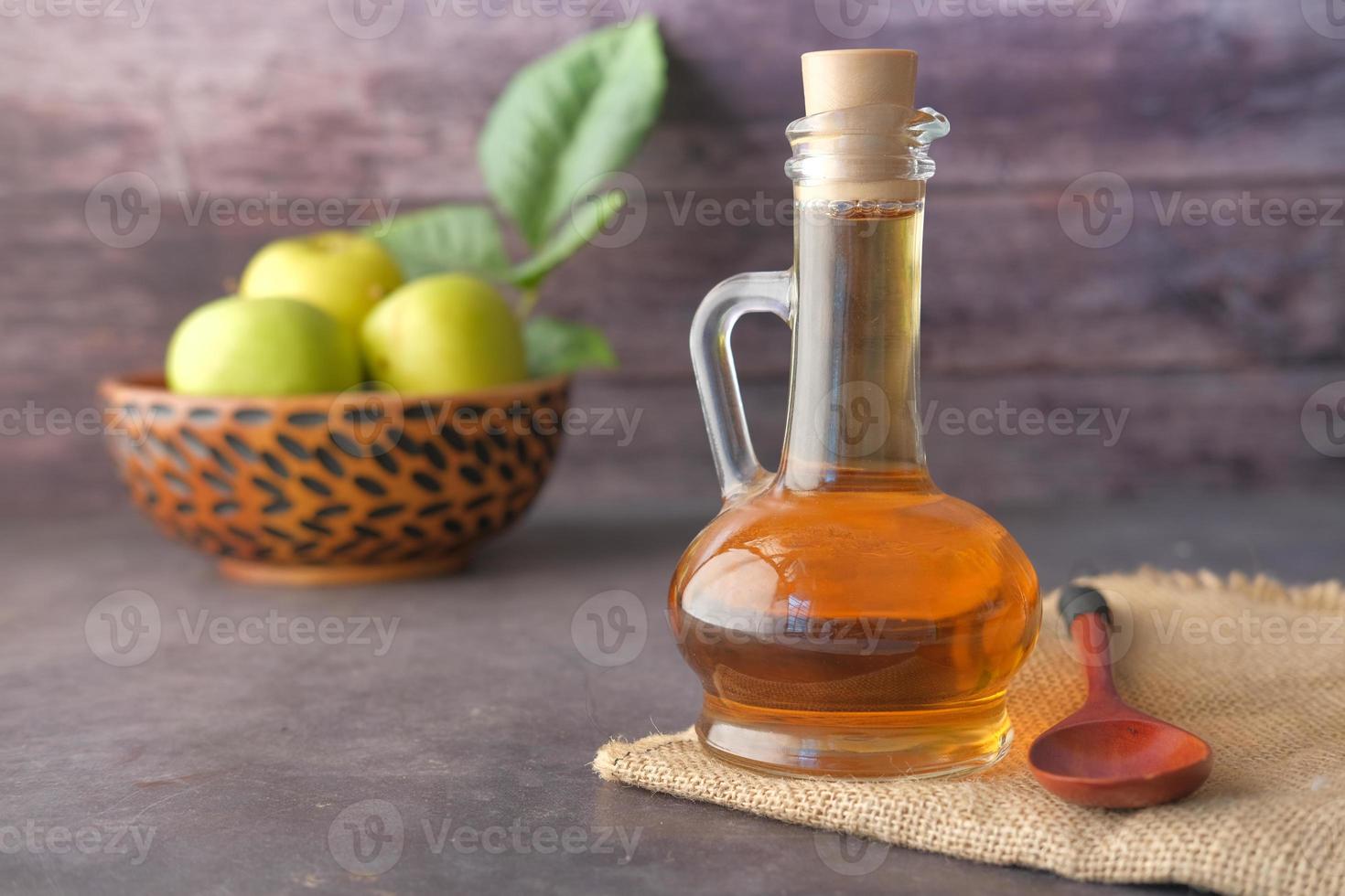 Vinagre de manzana en botella de vidrio con manzanas verdes frescas en la mesa foto