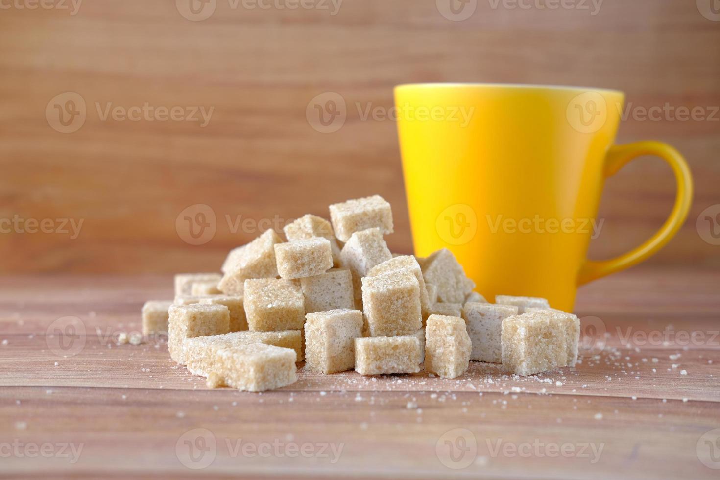 Taza de café amarilla y terrones de azúcar morena en la mesa foto