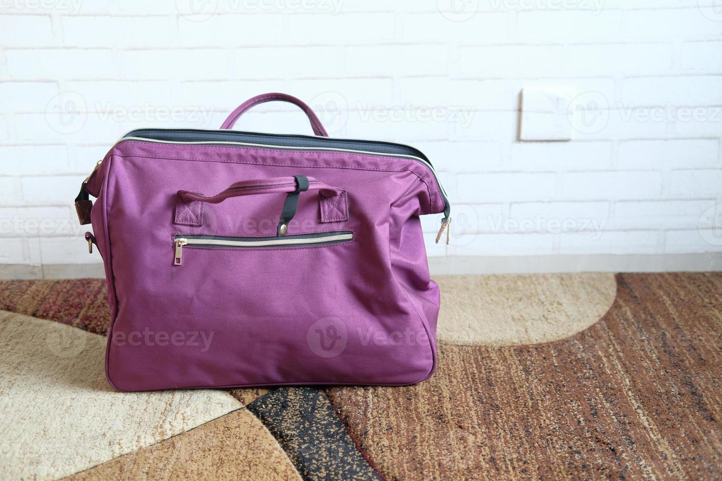 Purple travel bag on floor against a wall photo