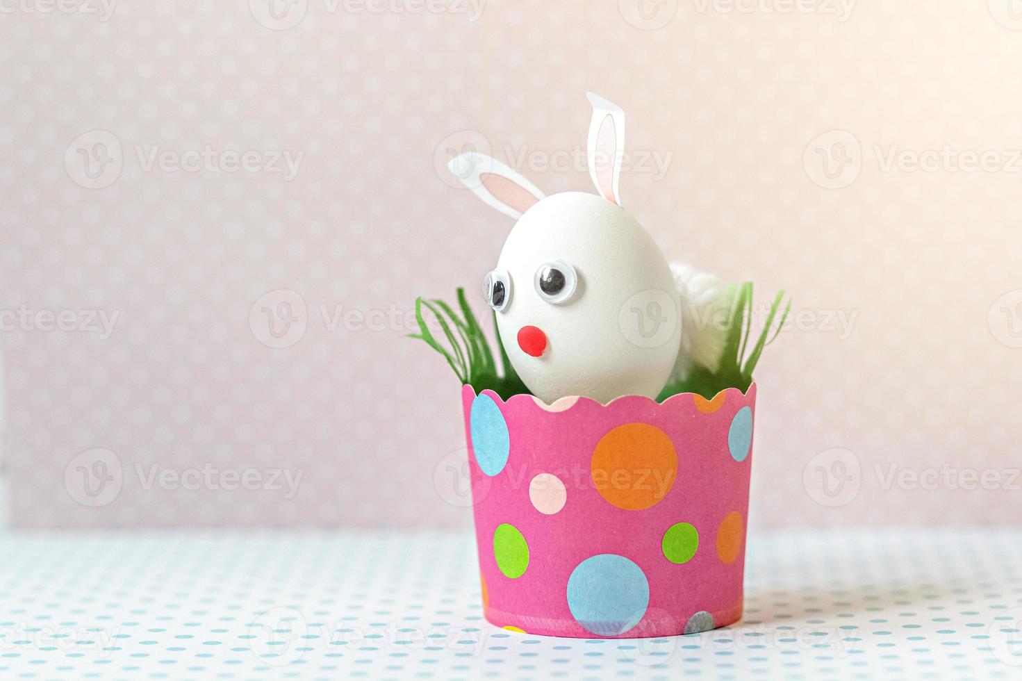 White chicken egg with bunny ears and a muzzle in an environmentally friendly pink paper tray photo