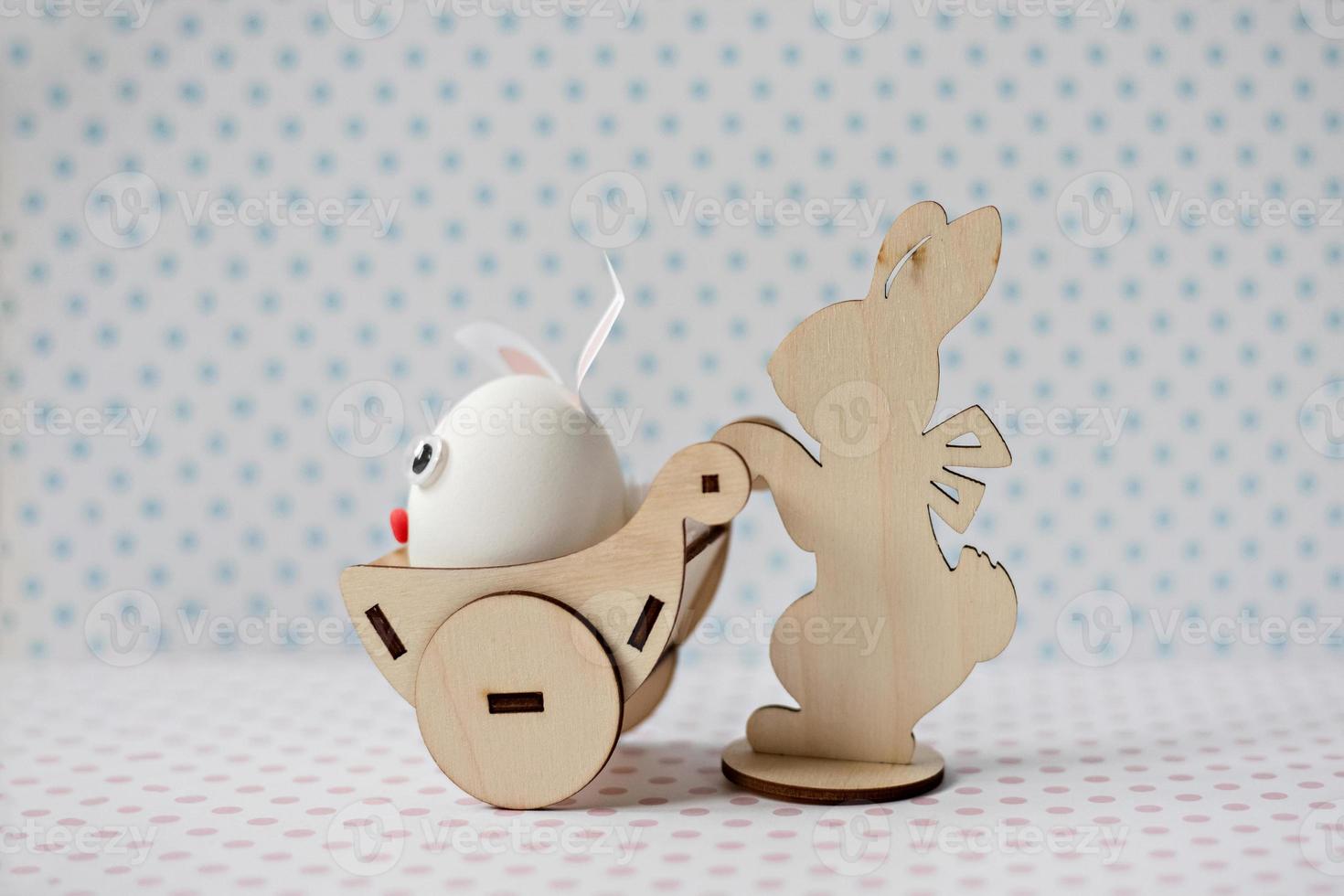 A wooden rabbit carries a cart with an egg with bunny ears photo